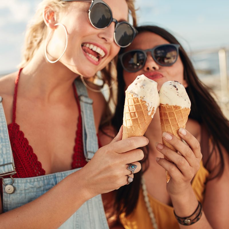 Portrait of two young women standing together eating ice cream. Happy young female friends outdoor.